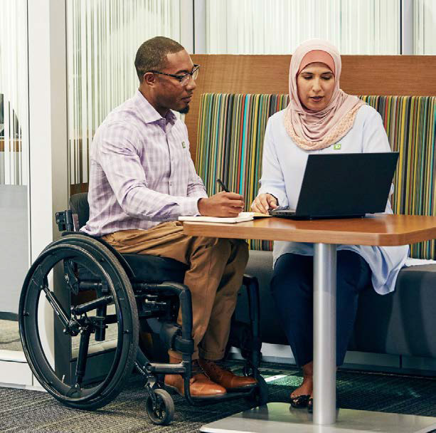 Man in wheelchair sitting with woman looking at laptop
